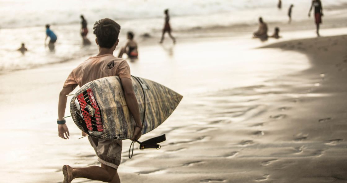 A Person Carrying A Surfboard On A Beach