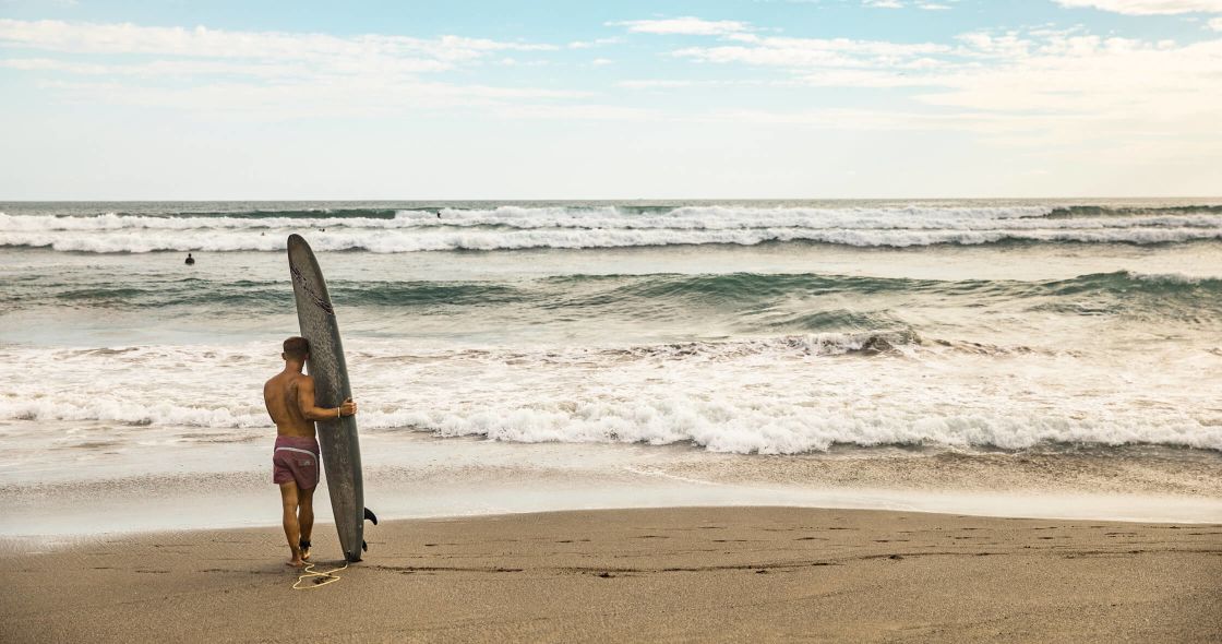 A Man Holding A Surfboard On A Beach