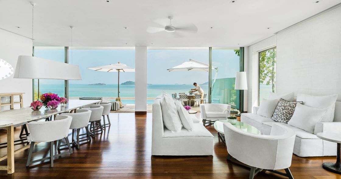 A Room With A Table Chairs And A Large Body Of Water