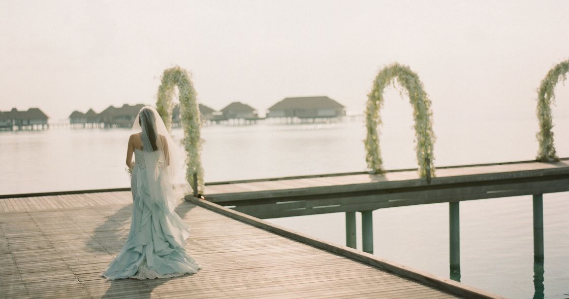 A Person In A White Dress Sitting On A Bench In Front Of A Body Of Water