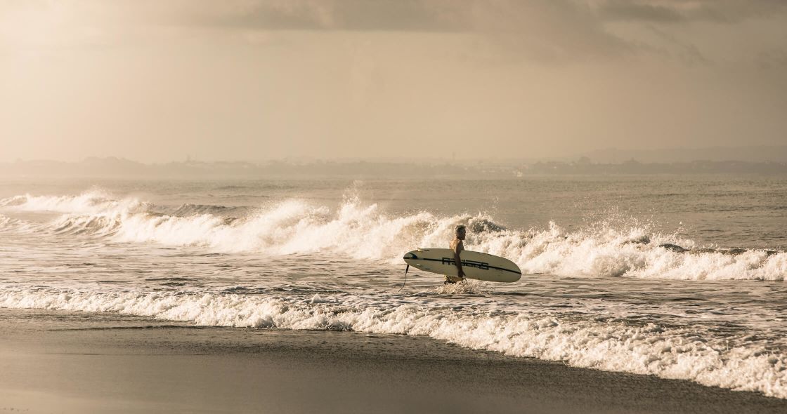 A Man Carrying A Surfboard On A Beach