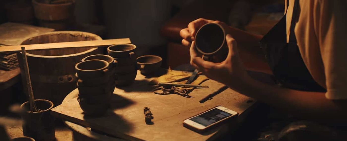 A Hand Holding A Phone Over A Table With Cups And A Hand Holding A Cell Phone