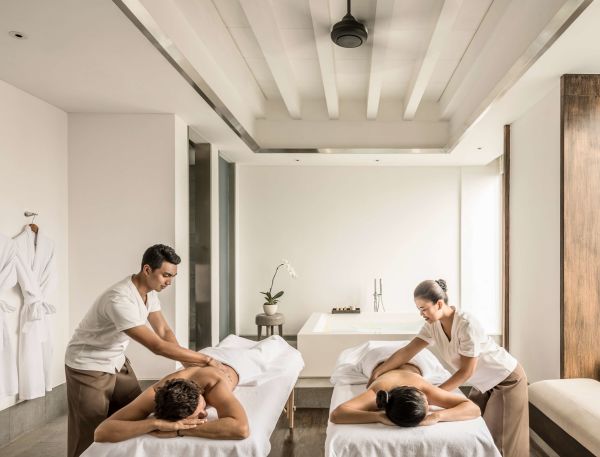A Man And Woman Sitting On A Bed In A Room With A Chandelier And A Couple