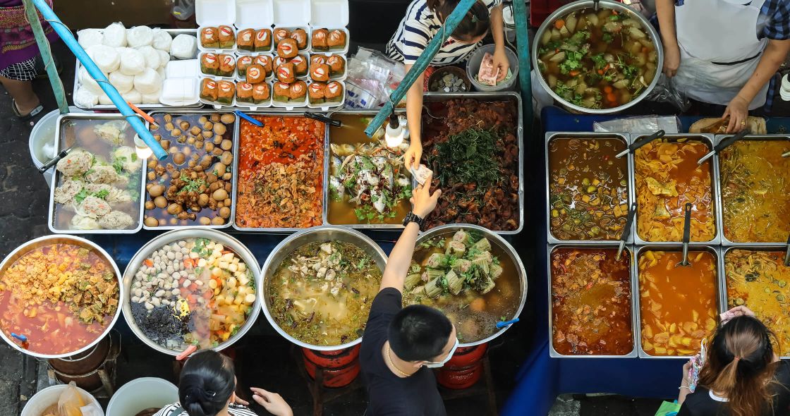 A Group Of People Standing Around A Table Full Of Food