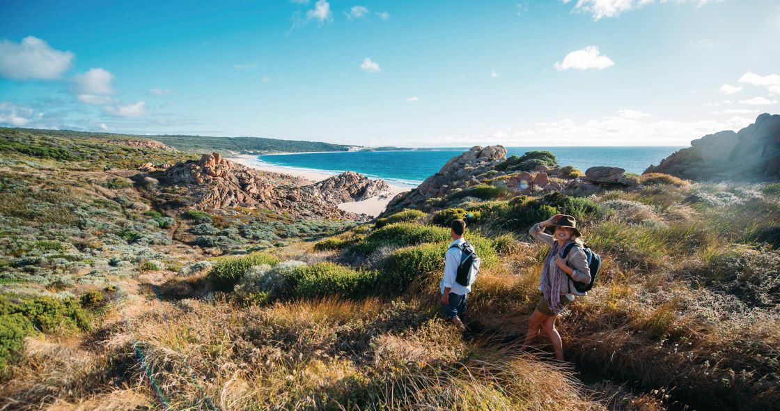 A Couple Of People Hiking On A Hill Overlooking A Body Of Water